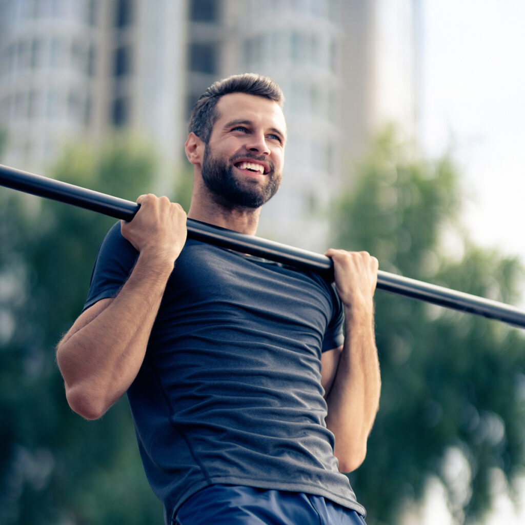 happy man, doing pulling up exercise at horizontal bar